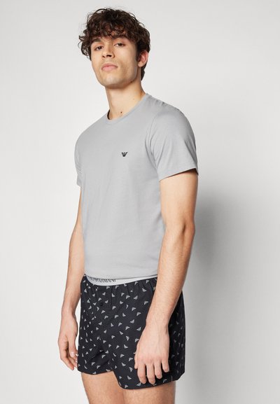 Graues Baumwoll-T-Shirt mit Rundhalsausschnitt und kleinem Logo. Schwarze gemusterte Boxer mit wiederkehrendem Design und elastischem Bund.