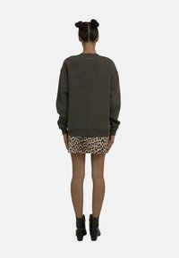 Sweatshirt oversize gris foncé avec un col ras du cou, associé à une jupe mini imprimé léopard et des bottines noires.