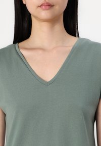 Grønn v-hals topp med korte ermer, glatt bomullsstoff og en avslappet passform. Har en minimalistisk design uten synlige mønstre eller detaljer.