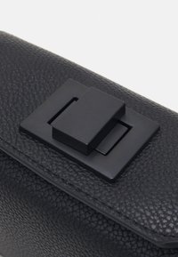 Patte de sac en cuir noir texturé avec un fermoir à pression rectangulaire noir mat centré dessus.