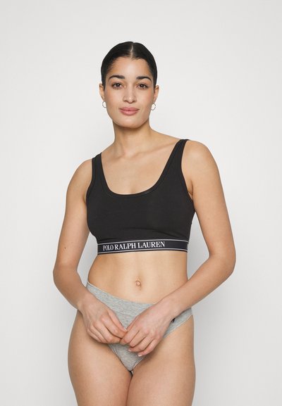 Black cropped sports bra with wide straps and a logo band; paired with gray low-rise briefs. Smooth fabric texture, simple design.