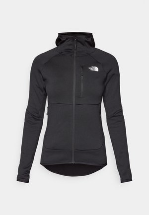 Chaqueta con capucha negra con cremallera, confeccionada en un material suave y elástico. Presenta un bolsillo frontal, mangas ajustadas y un logo en la parte superior izquierda.