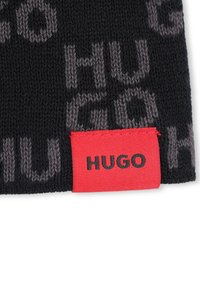 Accessorio lavorato a maglia nero con logo "HUGO" ripetuto in grigio. Etichetta rossa con "HUGO" in testo nero nell'angolo in basso a destra. Texture liscia.