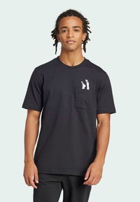 Μαύρο βαμβακερό μπλουζάκι με κοντό μανίκι, στρογγυλή λαιμόκοψη και τσέπη στο στήθος που διαθέτει μια λευκή, στυλιζαρισμένη γραφική απεικόνιση κάλτσας. Λείος υφασμάτινος ιστός.