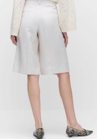 Ljusbeige culotter i slätt tyg, med hög midja, veck och två bakfickor, matchade med flats i ormskinnsmönster.