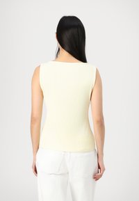 Ribbed, sleeveless top in soft yellow fabric with a crew neckline, paired with white, relaxed-fit trousers.