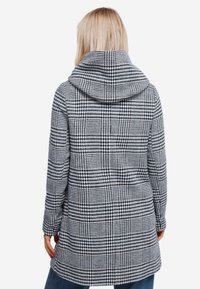 Hondstooth-gepatenteerde jas in zwart en wit, met een capuchon en lange mouwen, met een relaxte pasvorm en een middellange uitstraling.