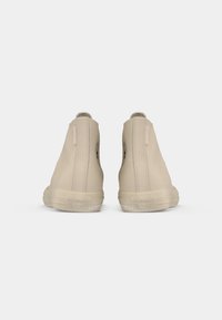 Beige hoge sneakers met een gladde canvas bovenkant, rubberen zool en een reliëflogo op de hiel. Voorzien van een ritssluiting aan de zijkant.