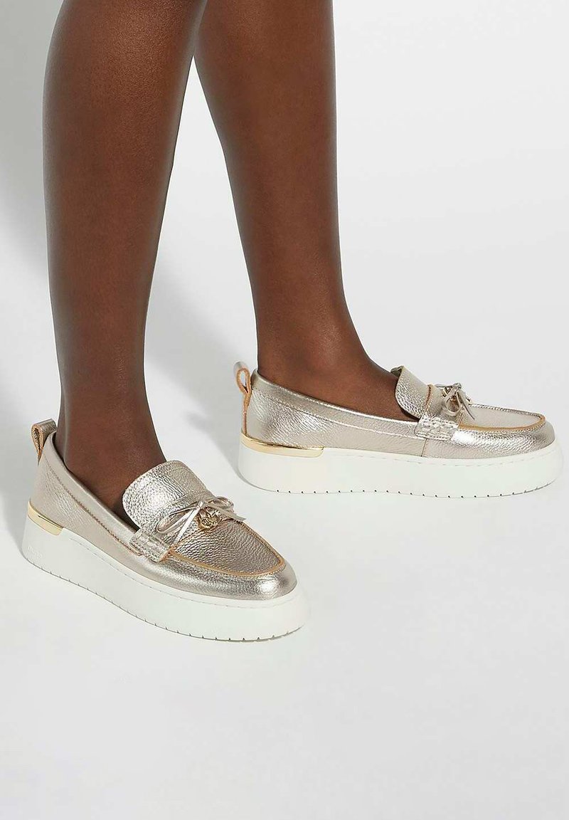 Metallic gold slip-on shoes with a textured finish, white sole, and decorative bow detail. Rounded shape and padded collar for comfort.