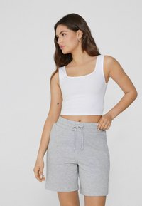 Weißes, geripptes Croptop mit quadratischem Ausschnitt, kombiniert mit grauen Strickshorts, die einen elastischen Bund und einen Kordelzug haben.