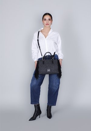 Zwarte fringe handtas van textuurstof, met dubbele handvatten en een afneembare schouderband, gecombineerd met een wit gestreepte shirt en blauwe jeans.