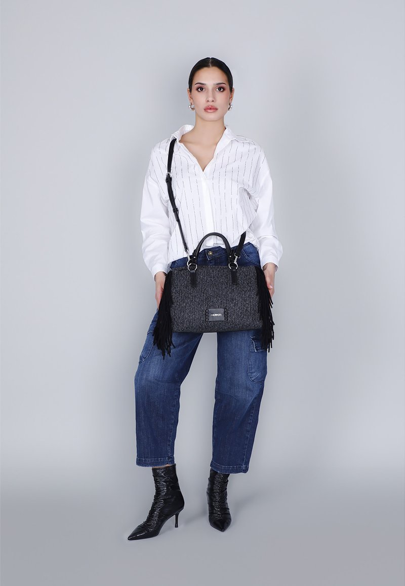 Borsa nera con frange realizzata in tessuto testurizzato, dotata di doppio manico e tracolla staccabile, abbinata a una camicia a righe bianche e jeans blu.