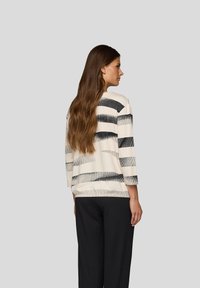 Langarmshirt in Beige mit schwarzen horizontalen Streifen, mit einer lockeren Passform und strukturiertem Stoff, kombiniert mit schwarzen strukturierten Hosen.