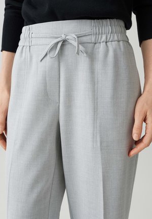 Partie médiane portant un pantalon gris clair avec une ceinture élastique et un cordon noué, associé à un haut à manches longues noir.