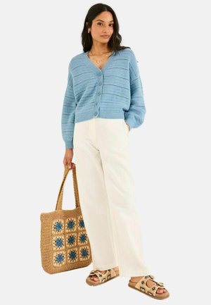 Hellblaues, lockeres Button-up-Cardigan, kombiniert mit weißen weit geschnittenen Hosen und einer gewobenen Tote-Tasche mit blauen Blumenakzenten.