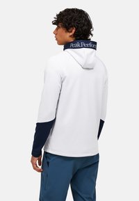 Kapuzensweatshirt in Weiß mit navyblauen Akzenten; verfügt über einen hohen Kragen und Logo-Details. Elegantes, körperbetontes Design mit glatter Textur.