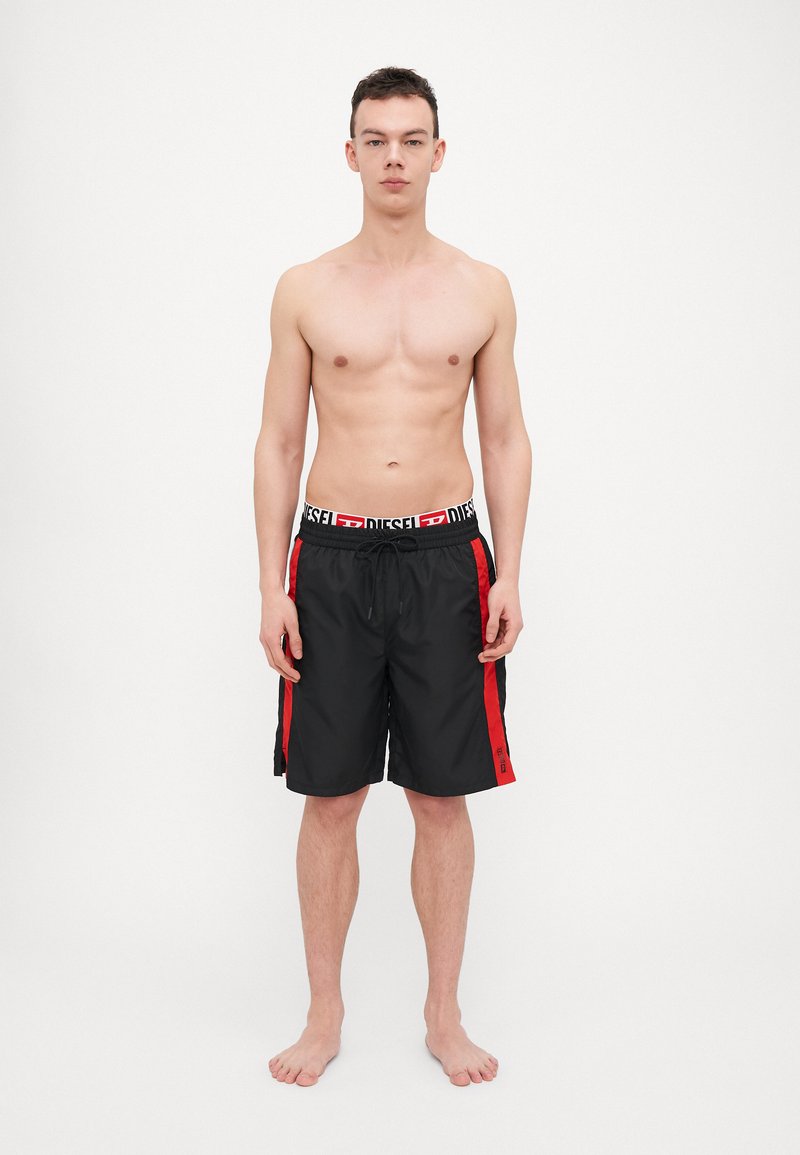 Black swim shorts with red side accents and drawstring waist, made of lightweight material. Features logo on waistband and lower hem.
