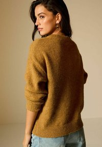 Senfgelbes Strickpullover mit lockerer Passform, gerippten Bündchen und Rundhalsausschnitt, kombiniert mit hellblauen hochtaillierten Jeans.