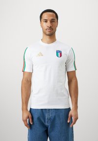 Λευκό βαμβακερό T-shirt με κοντά μανίκια, διακοσμημένο με πράσινες, κόκκινες και λευκές ρίγες, σήμα "Italia" και χρυσό λογότυπο Adidas στο στήθος.
