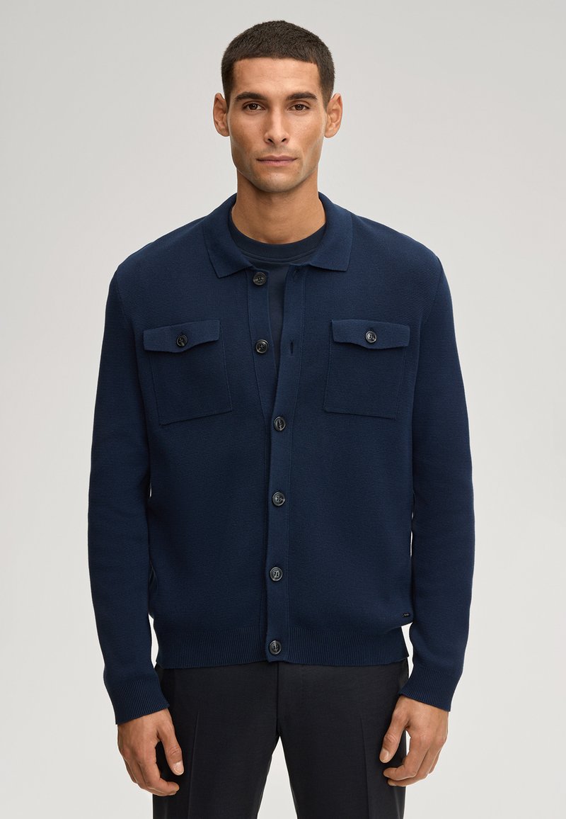 Cardigan bleu marine en tissu tricoté texturé, avec deux poches poitrine, fermeture à boutons et col. Coupe classique avec poignets côtelés.