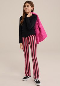 Fekete hosszúujjú póló, rózsaszín steppelt dzseki, rózsaszín, fekete és fehér csíkos trapéznadrág, fekete-fehér sportcipővel párosítva.