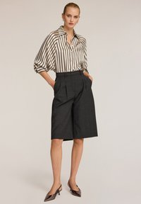 Mustat ja valkoiset raidalliset puserot, joissa on kaulus, yhdistetty tummaan räätälöityyn shortsit. Kiiltävät teräväkärkiset korot täydentävät asua.