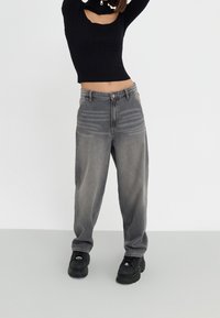 Jean gris taille haute, ample, avec un effet délavé et deux poches avant, associé à un pull court noir et des baskets épaisses noires.