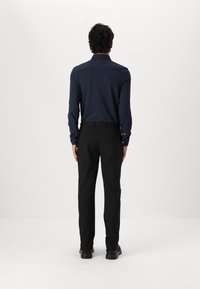 Námořnická košile s dlouhým rukávem a texturovaným vzorem, spárovaná s černými kalhotami a černými botami, viděná zezadu na bílém pozadí.