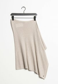 Beige stickad sjal hängande på en svart galge, med ett mönster med textur och en dekorativ detalj i ett hörn.