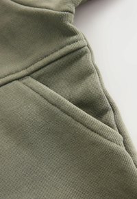 Tessuto verde oliva con una texture a righe, caratterizzato da un dettaglio di cucitura e un bordo leggermente ripiegato, che enfatizza la morbidezza e la flessibilità del materiale.