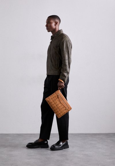 Veste bomber imprimée serpent marron, pantalon noir, mocassins noirs brillants et sac à main beige avec un motif logo texturé.