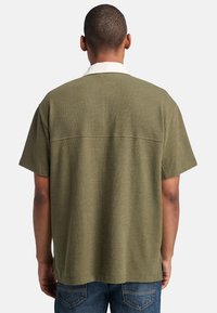 Kortärmad, olivgrön skjorta med vit krage. Texturerad tyg med rak skärning, med söm över ryggen. Bärs med denim.