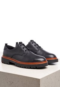 Scarpe in pelle nera con finitura liscia, punta rotonda e una soletta in legno. Presentano una suola in gomma testurizzata con profilo basso.