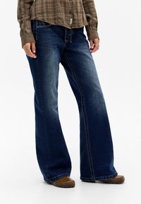 Dark blue denim wide-leg jeans with subtle fading, a mid-rise waist, and contrasted stitching. Paired with a brown plaid shirt and brown shoes.