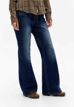 Dark blue denim wide-leg jeans with subtle fading, a mid-rise waist, and contrasted stitching. Paired with a brown plaid shirt and brown shoes.