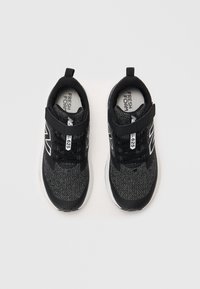 Baskets de sport noires avec un upper en tricot texturé, dotées d'une bande auto-agrippante et d'une semelle extérieure blanche. Comprend un logo sur les côtés.