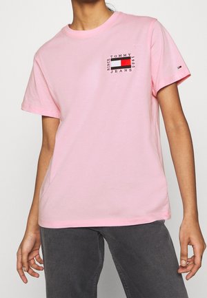 Roze katoenen T-shirt met korte mouwen, met een klein grafisch embleem met "TOMMY JEANS" en een rechthoekig ontwerp in rood, wit en blauw.