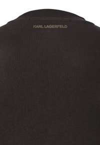 Tissu de vêtement noir avec l'inscription "KARL LAGERFELD" en petites lettres dorées près de l'encolure arrière supérieure.