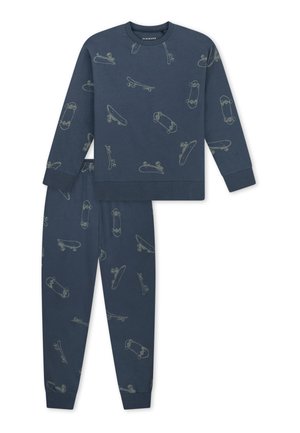 Smiling boy standing barefoot wearing matching dark blue pajamas with light skateboard patterns on top and pants.