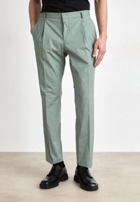 Pantalon vert clair avec une devant plissé, poches lat�érales et une coupe cintrée. Associé avec des chaussures noires à lacets. Texture de tissu lisse.