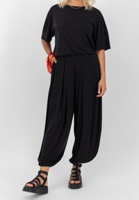 Svart löstsittande t-shirt, i kombination med tapered, veckade svarta byxor med fickor och en broderad hjärtdetalj. Svarta remsandaler.