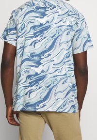 Camicetta a maniche corte con un motivo marmorizzato fluido in blu, bianco e verde chiaro. Realizzata in tessuto leggero con una vestibilità rilassata.