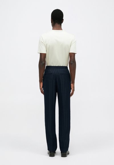 Šviesiai rudas trumpas rankovėmis marškinėliai ir tamsiai mėlyni, tekstūruoti plačios kojų kelnės, su išryškintu juosmeniu ir tiesiu siluetu. Subtilus dryžuotas raštas.