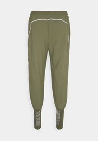 Pantalon de jogging fuselé vert olive avec taille élastique, détails en piping blanc et poignets côtelés arborant le texte "NIKE F.C.".