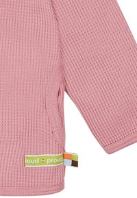 Maglia rosa a trama waffle con maniche lunghe, tasche laterali e un’etichetta verde e multicolore che recita "loud + proud."