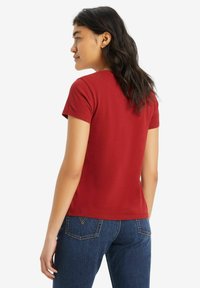T-shirt rossa in cotone con maniche corte, scollo rotondo e vestibilità aderente, abbinata a jeans in denim blu scuro.