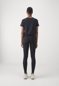 Czarna koszulka i czarne legginsy o gładkiej teksturze, z małym logo na nodze, zestawione z jasnymi butami sportowymi.