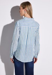 Camicia a righe in lino blu chiaro e crema, con maniche lunghe, polsini abbottonati e orlo curvo sul retro. Presenta una piega e uno yoke posteriore.