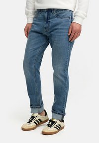 Lyseblå denimjeans med rett ben, med frontlommer og oppbrettede mansjetter, kombinert med beige og svarte sneakers.