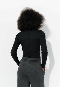 Haut noir à manches longues avec un design ajusté, associé à un pantalon à carreaux taille haute avec une taille élastique et des poches latérales.